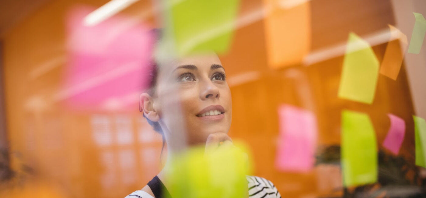 Mujer joven analizando ideas en post-its de colores en una pared de cristal, ejemplo de desarrollo de competencias digitales y blandas en la Universidad Anáhuac Oaxaca.
