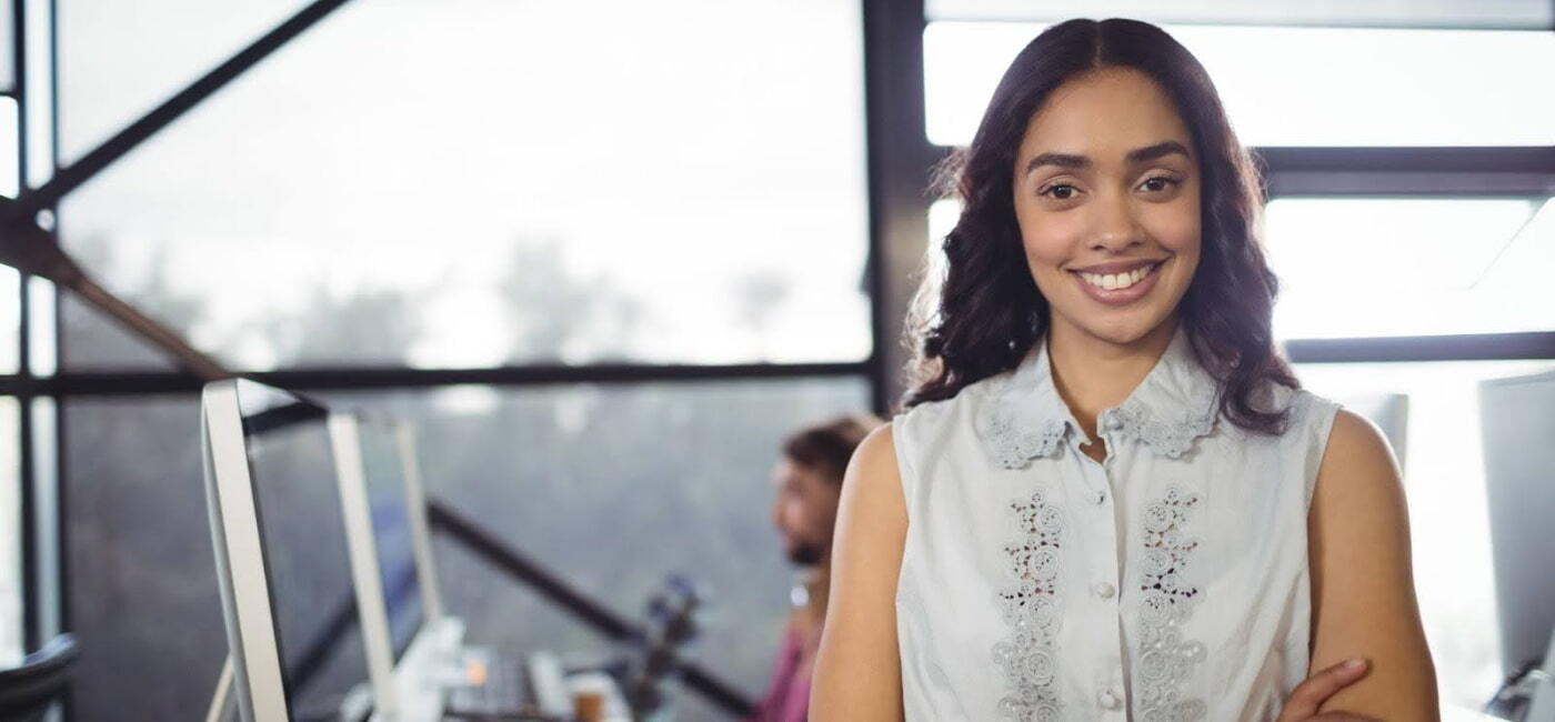 Estudiante universitaria sonriente en oficina moderna, lista para comenzar sus prácticas profesionales en un entorno laboral tecnológico.