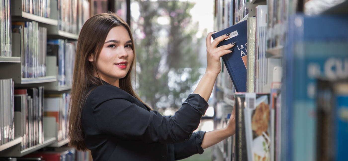 Estudiante en biblioteca seleccionando un libro, representando la búsqueda de conocimiento y elección de una carrera con futuro en Oaxaca.