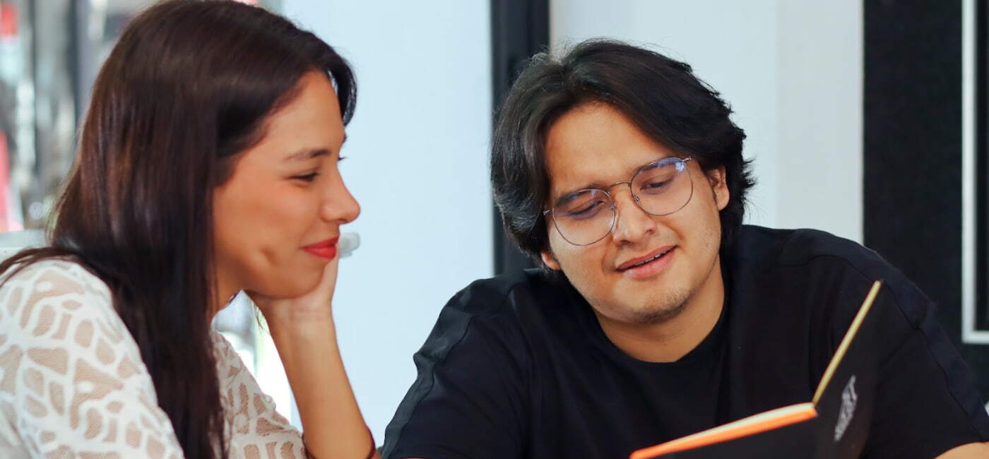 Dos estudiantes conversando y revisando un cuaderno juntos, ilustrando la colaboración y el ambiente académico en universidades de Oaxaca.